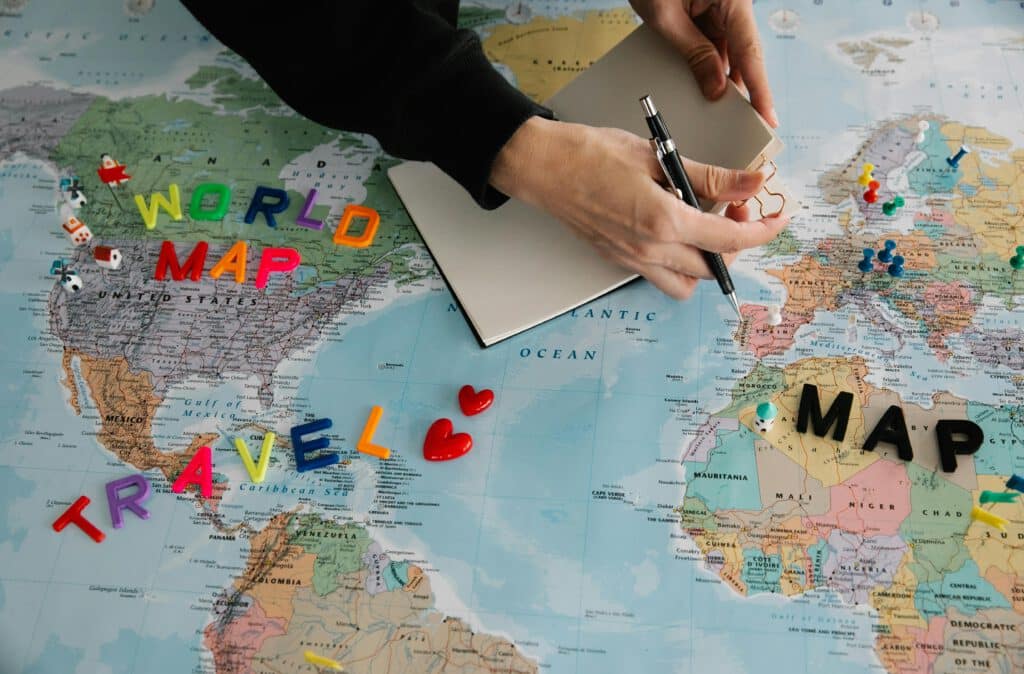 Handen die een wereldkaart onderzoeken met kleurrijke letters en reissymbolen.