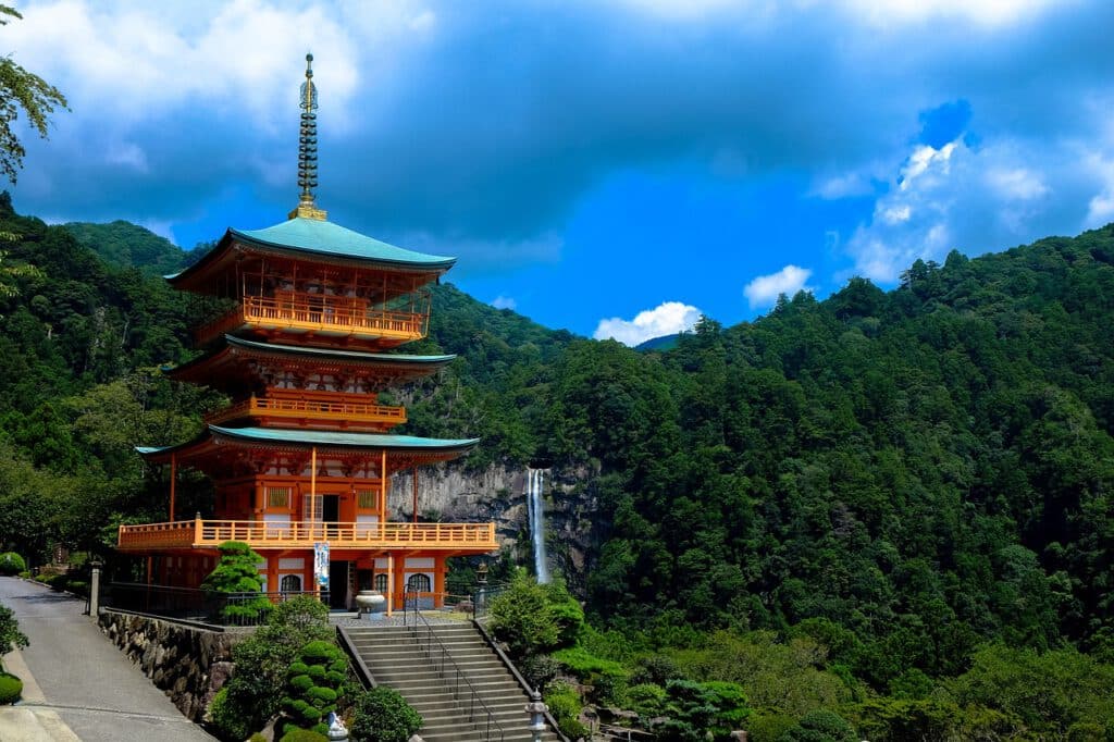 Traditionele Japanse pagode omringd door weelderige groene bergen en een waterval op de achtergrond.