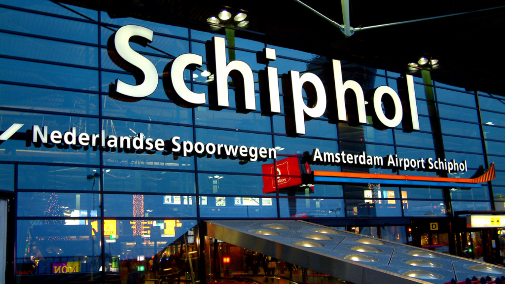 Ingang van Amsterdam Airport Schiphol met prominente verlichte borden, die de eenvoudige toegang tot internationale vluchten met Vlucht-Ticket.nl benadrukt.