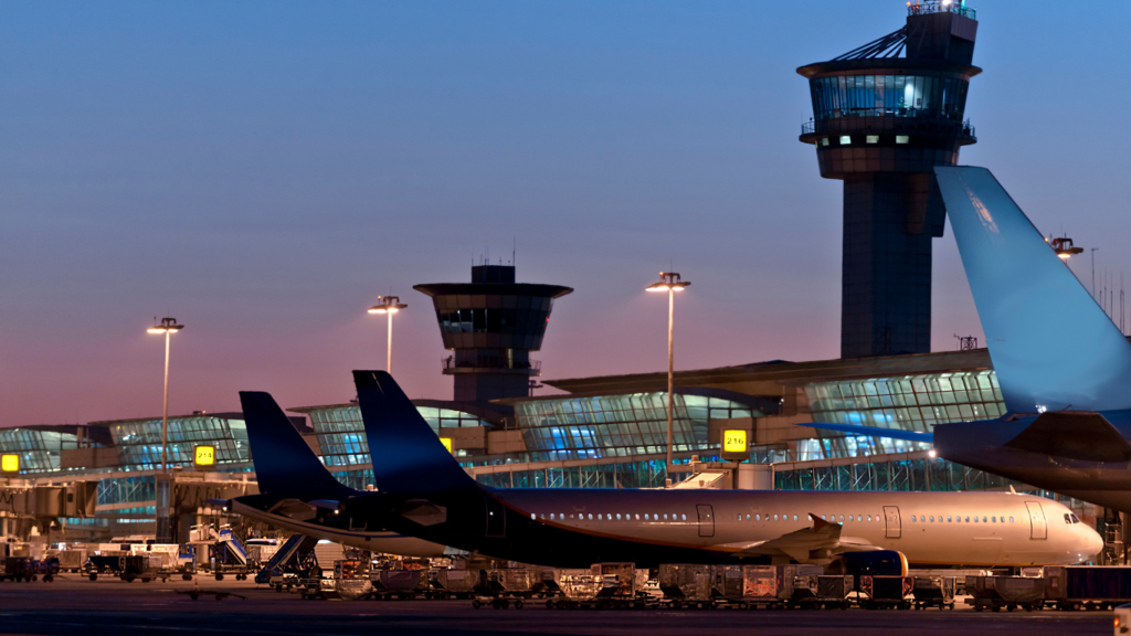 Vliegtuig geparkeerd bij de luchthaven tijdens de schemering, met de verkeerstorens op de achtergrond, wat de professionaliteit en efficiëntie van Vlucht-Ticket.nl weerspiegelt.