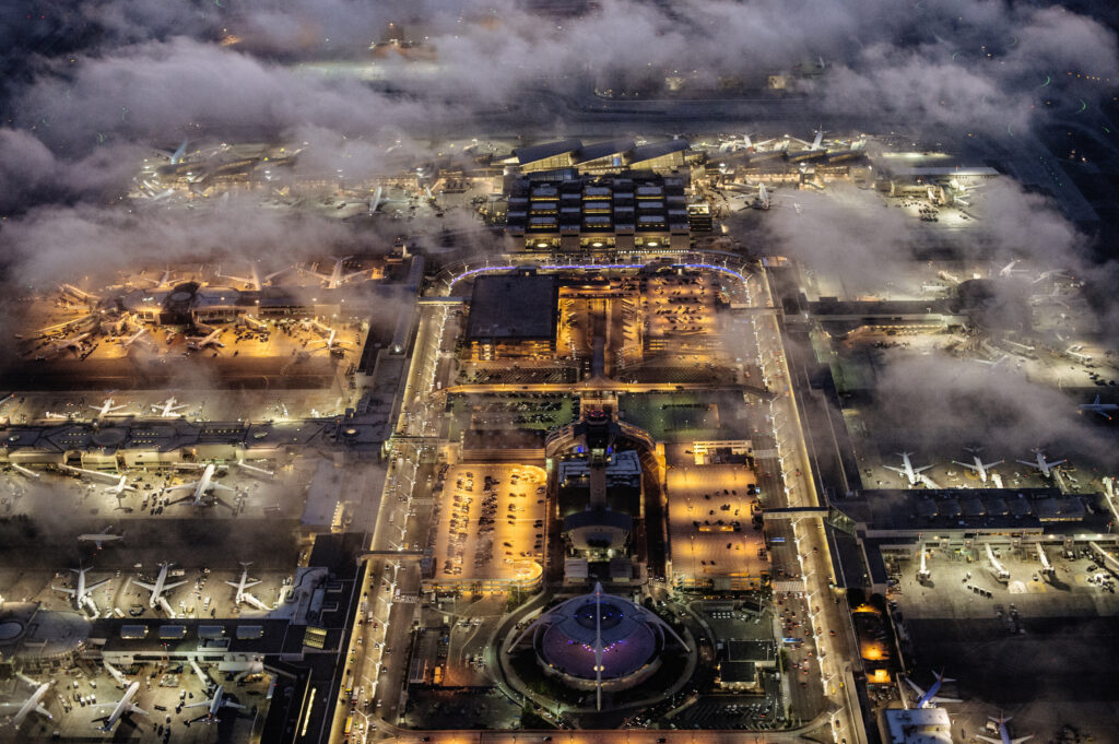 Luchthaven vanuit de lucht bij nacht, met verlichte terminals en vliegtuigen, perfect voor vluchten vanuit Amsterdam naar Londen.