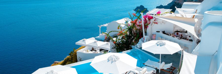 Uitzicht op een luxe hotel met zwembad en terras aan de kust van Santorini, perfect voor hotelvergelijkingen via Vlucht-Ticket.nl.