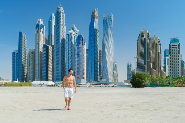 Man wandelt over het strand in Dubai, met de moderne skyline op de achtergrond, ideaal voor een luxe last minute reis.